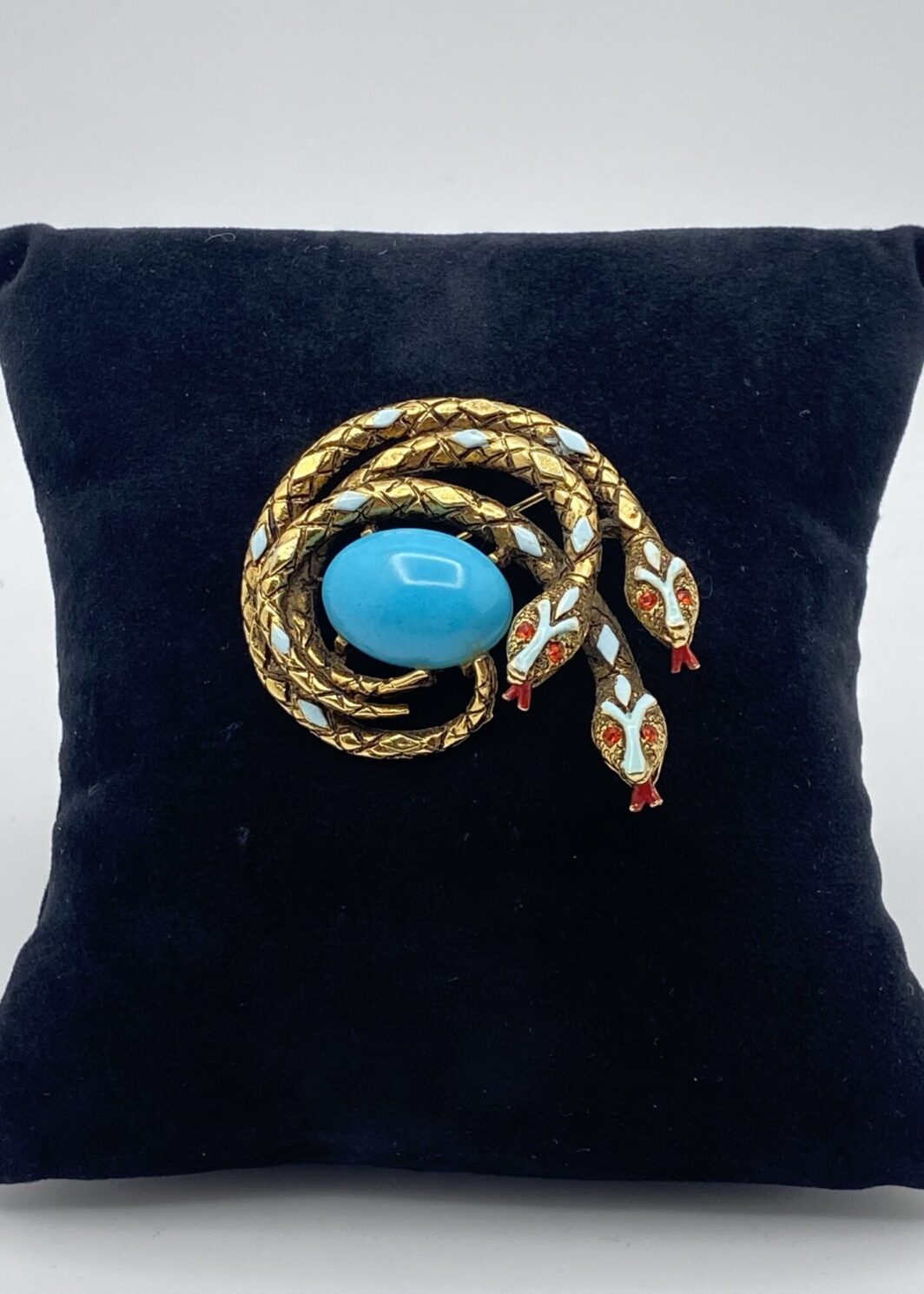 “ART”. STRAORDINARIA SPILLA CON TRE SERPENTI, IN METALLO GOLDTONE, SMALTI E CENTRALE IN PASTA DI VETRO COLOR TURCHESE. BIGIOTTERIA AMERICANA VINTAGE ANNI ‘60.