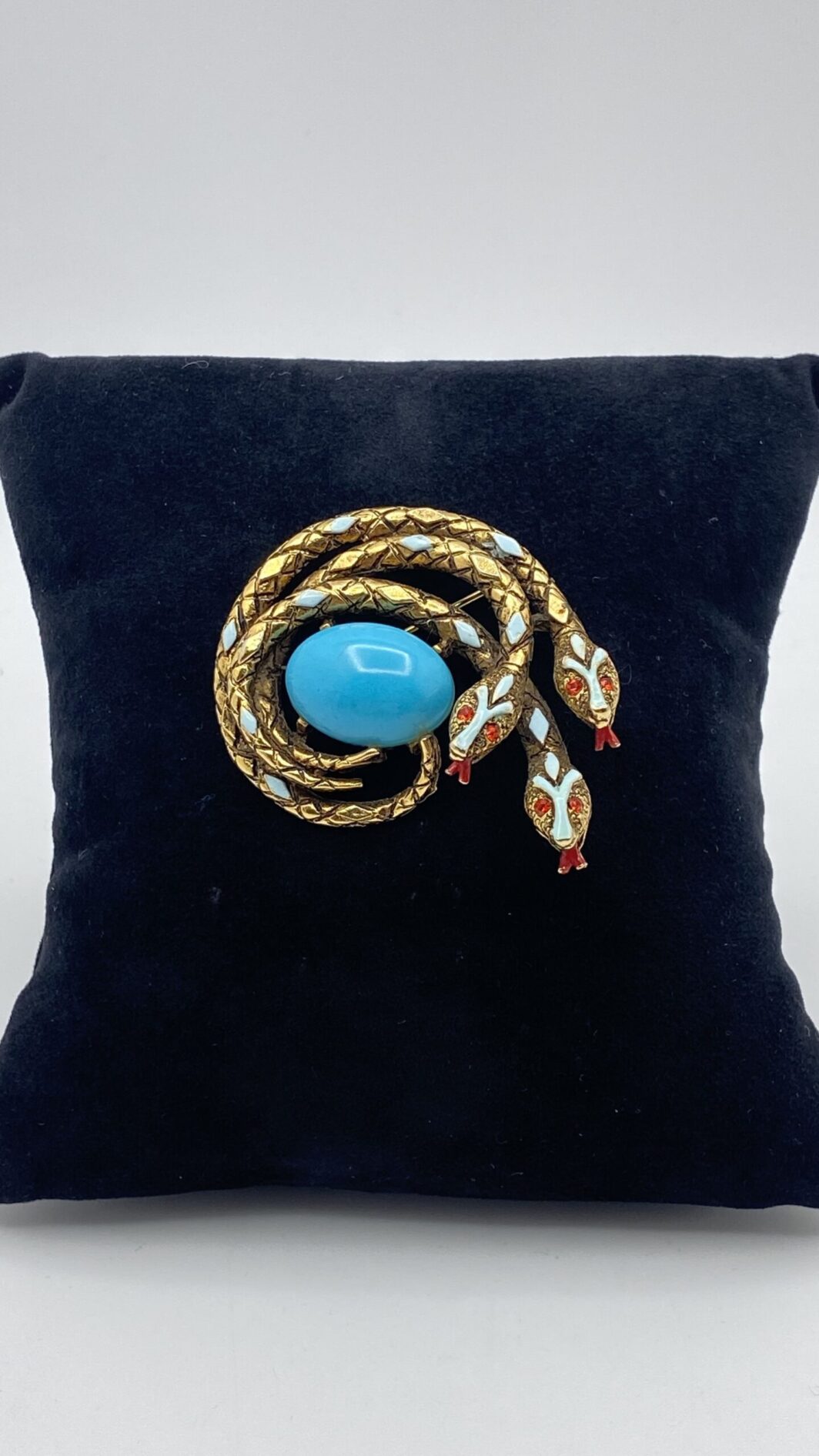 “ART”. STRAORDINARIA SPILLA CON TRE SERPENTI, IN METALLO GOLDTONE, SMALTI E CENTRALE IN PASTA DI VETRO COLOR TURCHESE. BIGIOTTERIA AMERICANA VINTAGE ANNI ‘60.