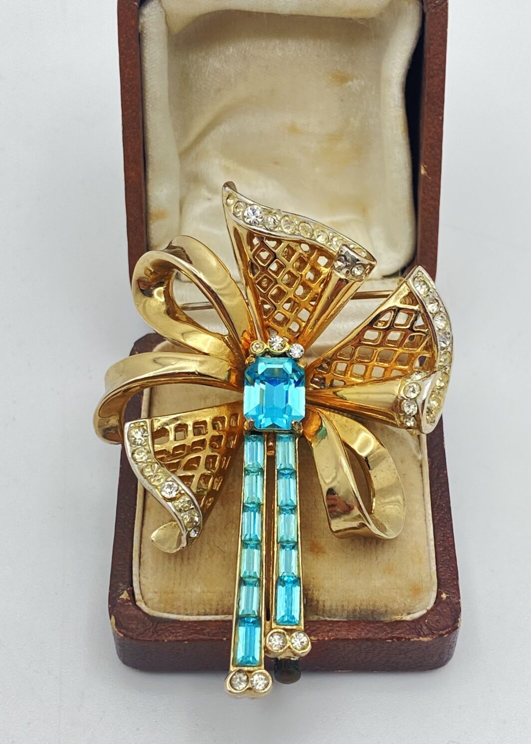 MAGNIFICA SPILLA VINTAGE ANNI’30/’40 FIRMATA CORO CRAFT – METALLO DORATO, FINEMENTE SAGOMATO A FORMA DI FIOCCO CON NAPPE, ARRICCHITO DA STRASS LUMINOSI E CRISTALLI ACQUAMARINA TAGLIO BAGUETTE.