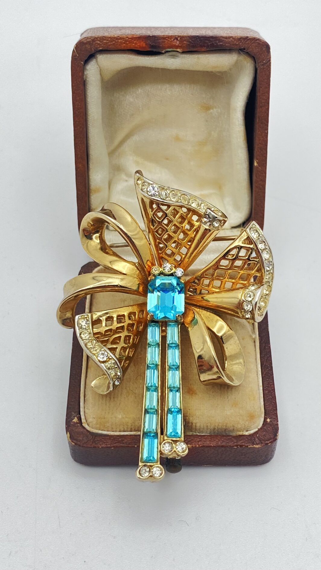 MAGNIFICA SPILLA VINTAGE ANNI’30/’40 FIRMATA CORO CRAFT – METALLO DORATO, FINEMENTE SAGOMATO A FORMA DI FIOCCO CON NAPPE, ARRICCHITO DA STRASS LUMINOSI E CRISTALLI ACQUAMARINA TAGLIO BAGUETTE.