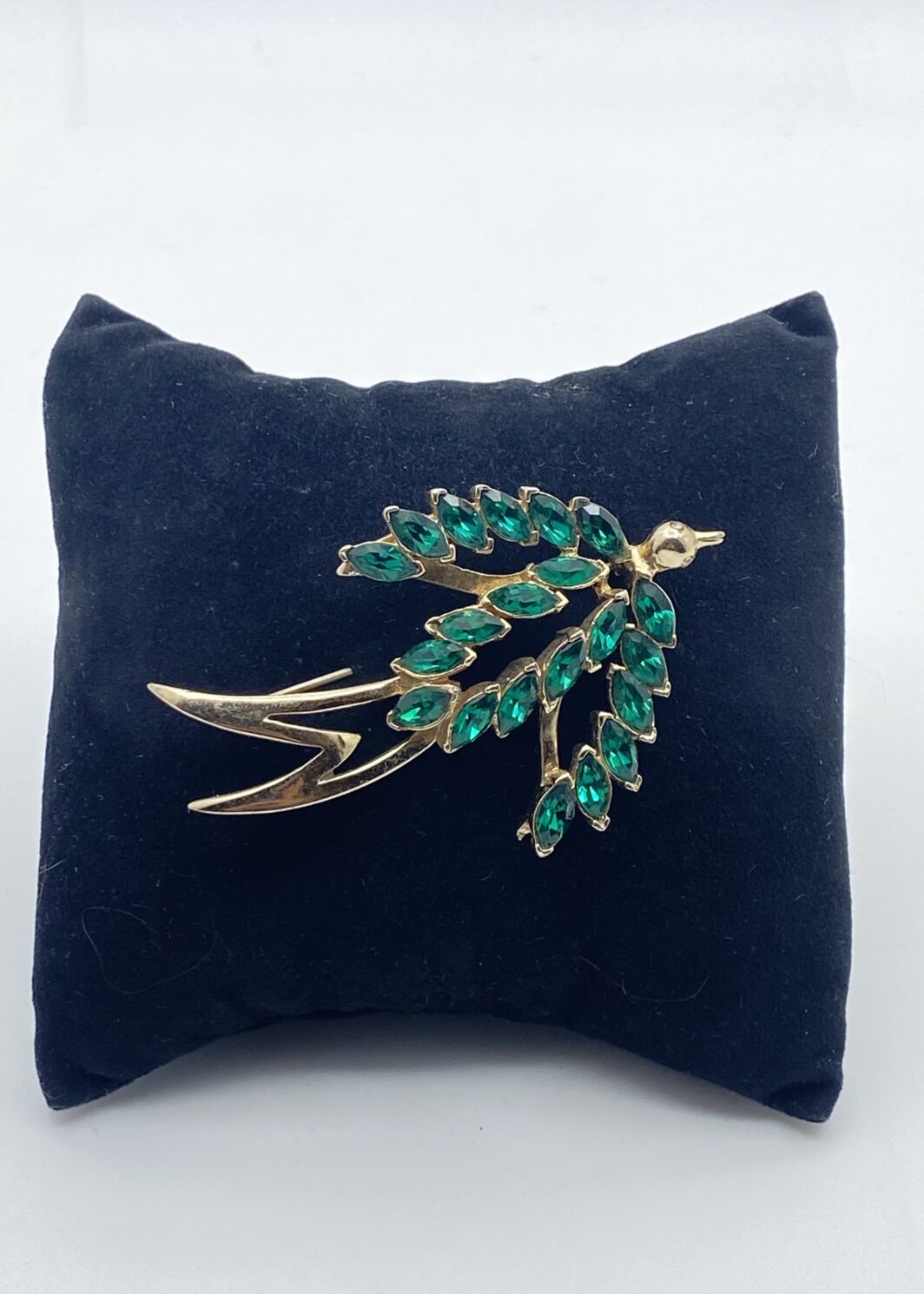 SPILLA FIRMATA “CORO CRAFT”. RONDINE IN METALLO GOLDTONE CON CRISTALLI VERDI E OCCHI CON STRASS DIAMOND-LIKE. BIGIOTTERIA AMERICANA ANNI’30/‘40.