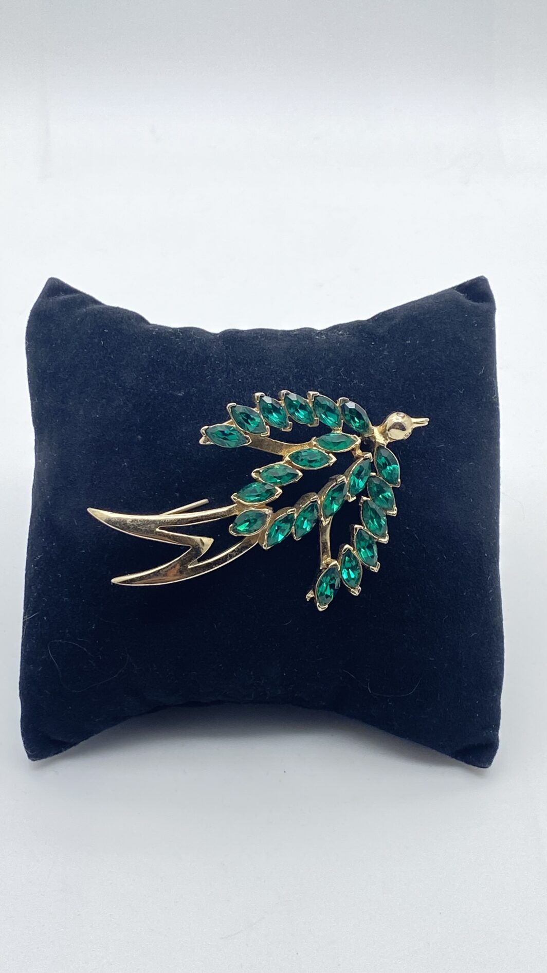 SPILLA FIRMATA “CORO CRAFT”. RONDINE IN METALLO GOLDTONE CON CRISTALLI VERDI E OCCHI CON STRASS DIAMOND-LIKE. BIGIOTTERIA AMERICANA ANNI’30/‘40.
