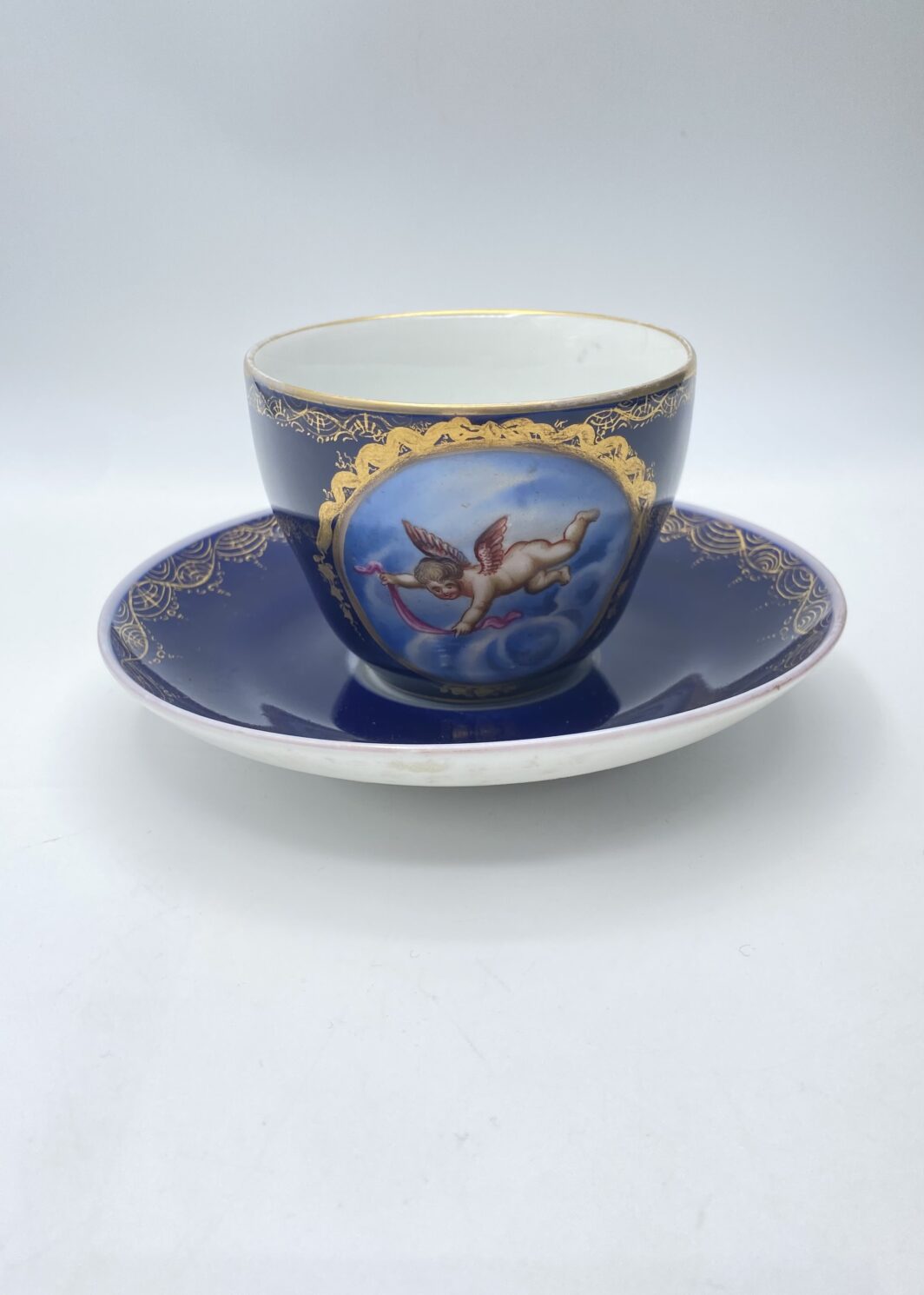 ECCEZIONALE TAZZA CON PIATTINO IN PORCELLANA BLU COBALTO, MEDAGLIONE CON PUTTO E ORO ZECCHINO – REALE MANIFATTURA KPM BERLINO, XVIII SECOLO.