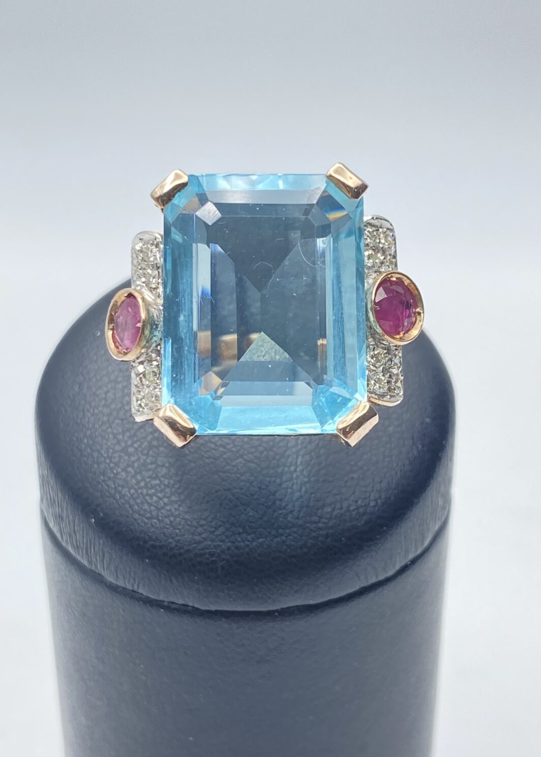 ELEGANTE ANELLO IN STILE ART DÉCO IN ORO ROSA CON TOPAZIO AZZURRO DA 10 CARATI, 0,80 ct DI RUBINI E 0,50 ct DI DIAMANTI TAGLIO BRILLANTE
