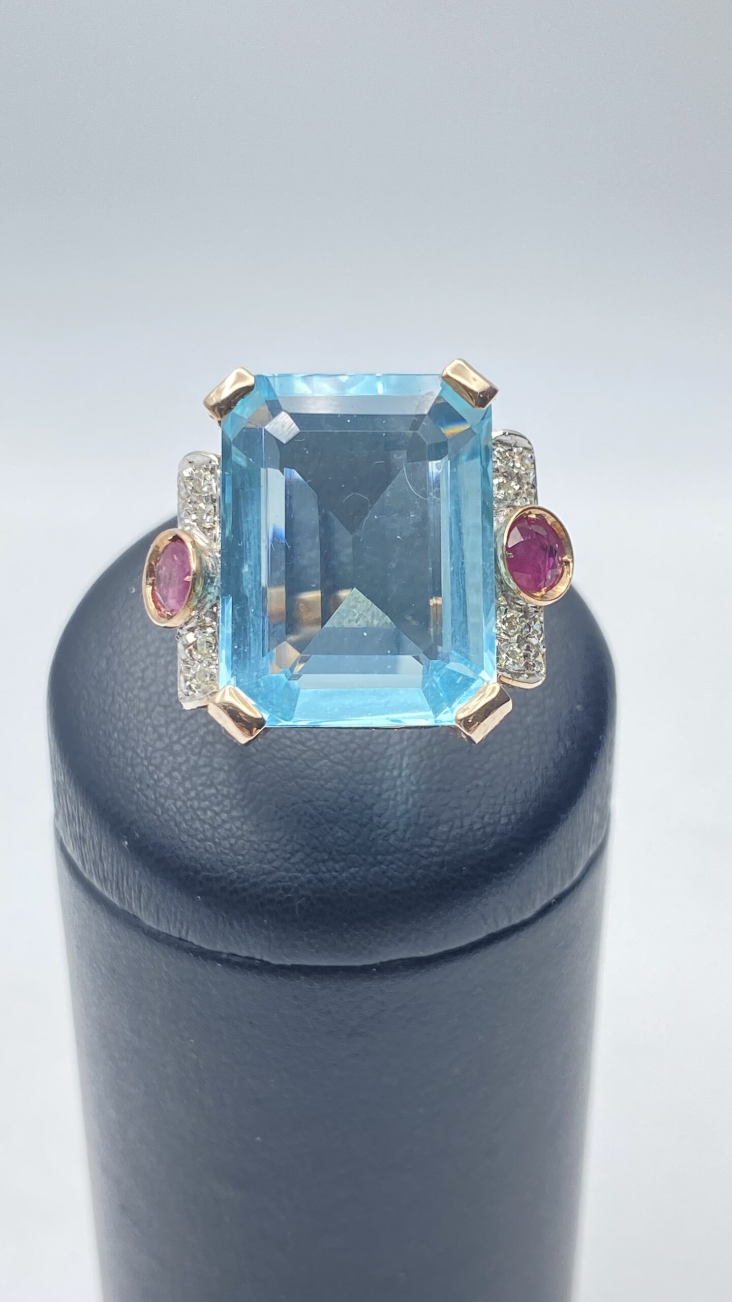 ELEGANTE ANELLO IN STILE ART DÉCO IN ORO ROSA CON TOPAZIO AZZURRO DA 10 CARATI, 0,80 ct DI RUBINI E 0,50 ct DI DIAMANTI TAGLIO BRILLANTE